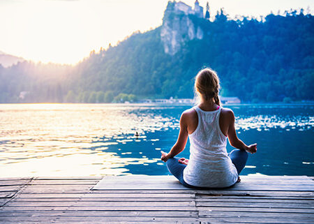Frau im Meditationssitz mit Ausblick auf einen See