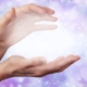Hands cupped around light on a background of blues and purples.